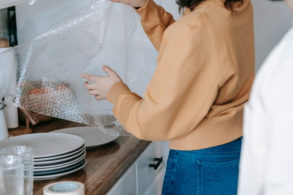 Adult woman carefully wrapping dishes in bubble wrap for packing in kitchen setting.
